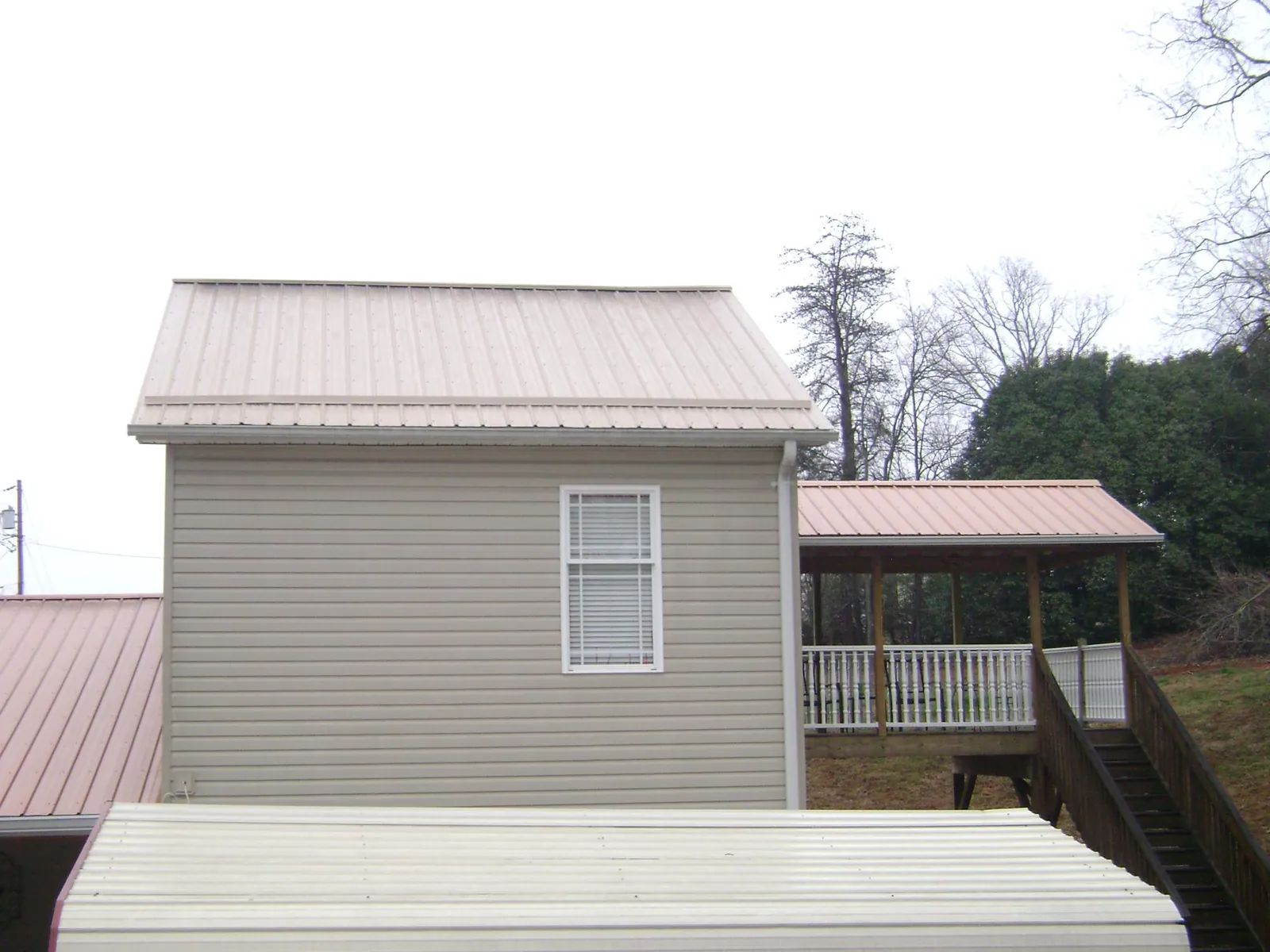Tan metal roofs on a two story addition and attached porch, from a Roof Replacement job in Paris